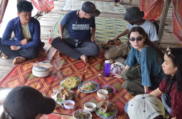 A group of young people sitting on a blanket on a floor eating food together