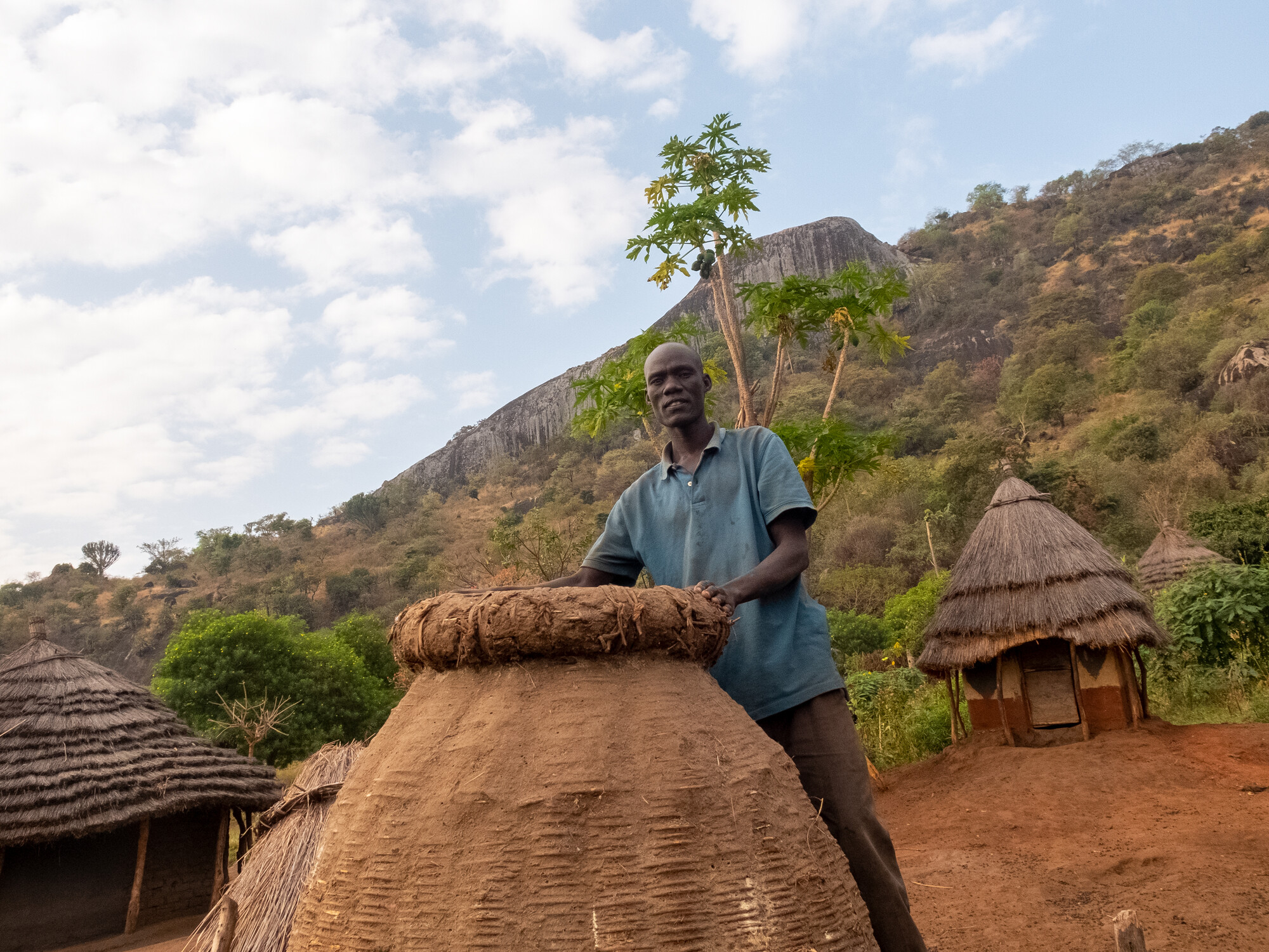 A man stands behind a traditional Ugandan granary 