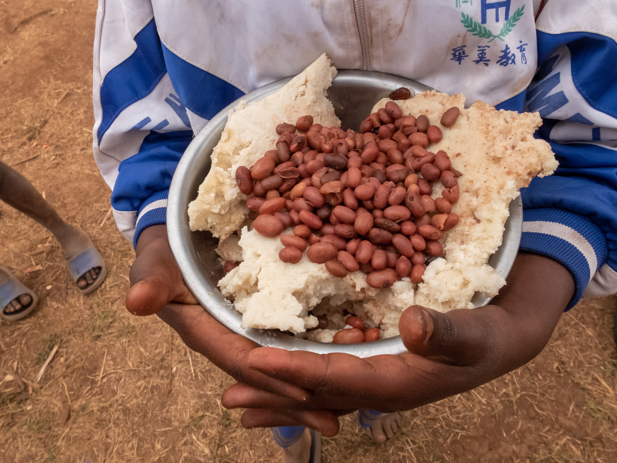 A Ugandan child holding a bowl of cooked maize and beans