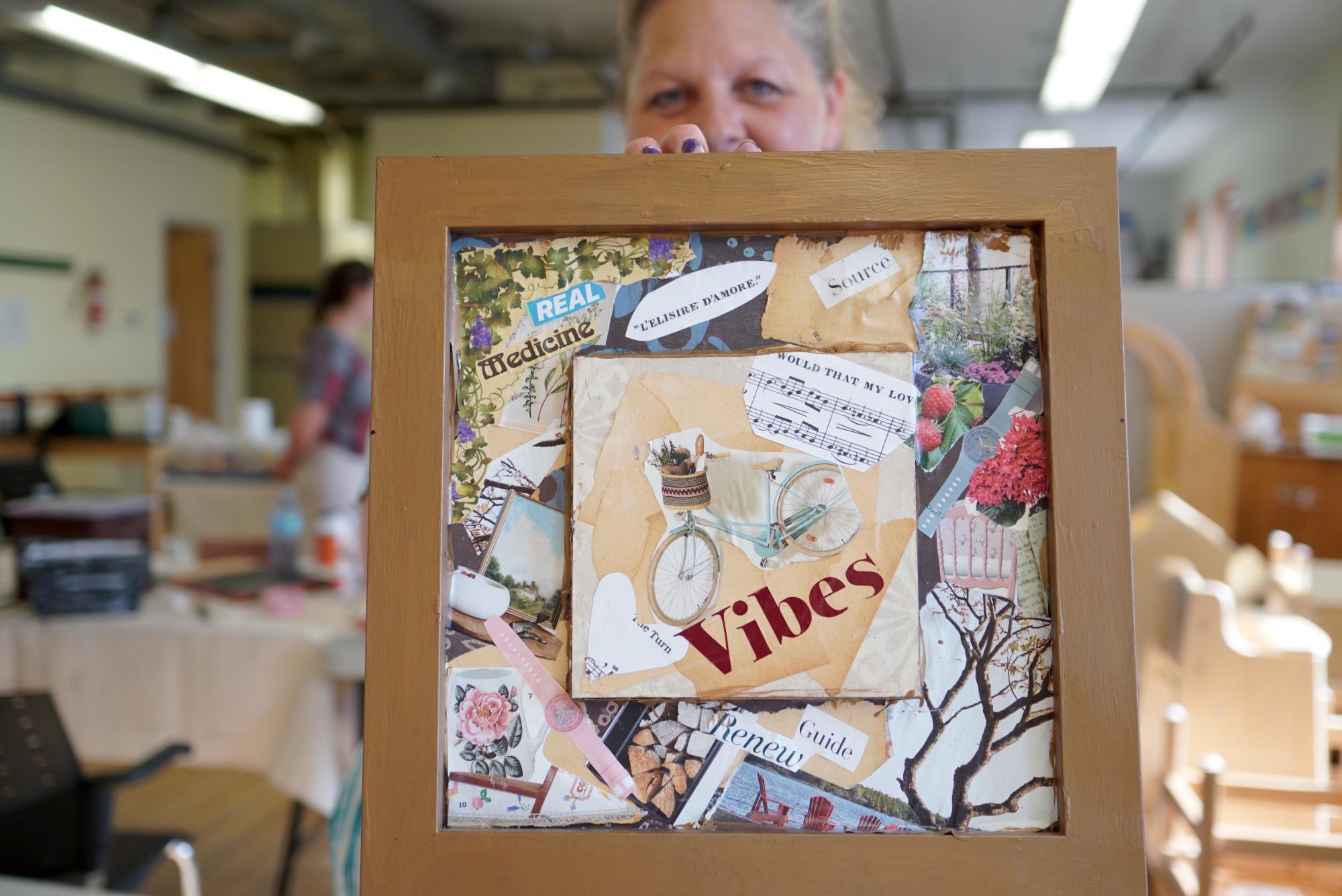 A woman holds up a framed collage with positive messages on it.