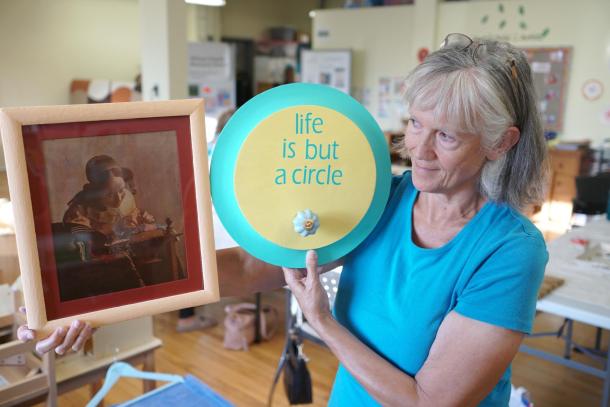 A woman in a blue shirt holds ups a plate that reads, "Life is but a circle."