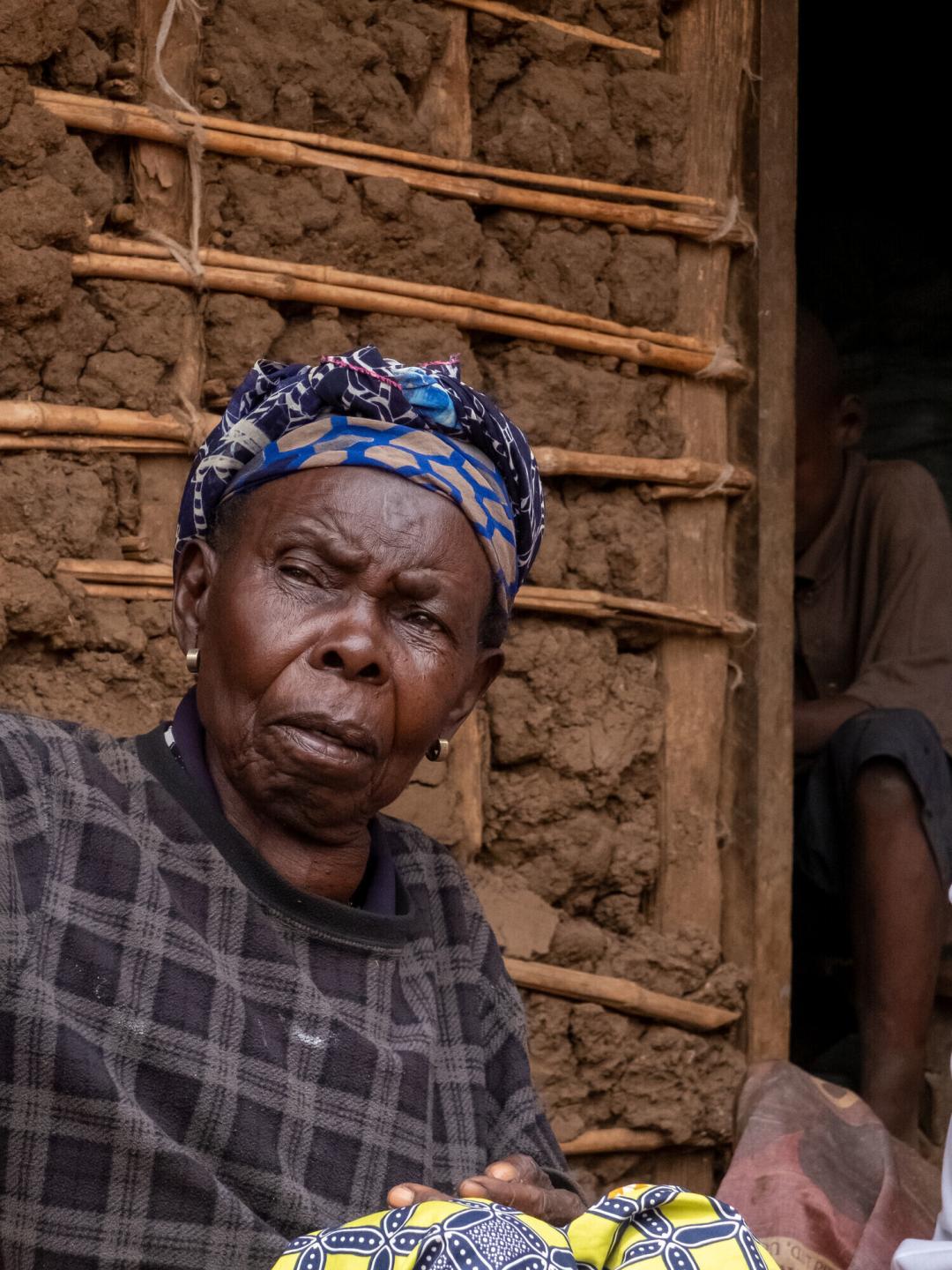 An elder Uganda woman sits by a mud brick wall