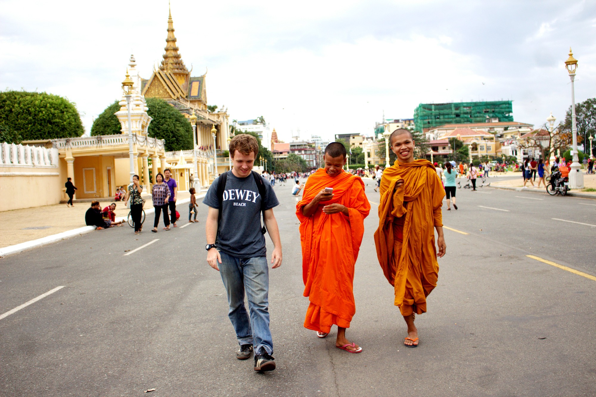 A young man and two Buddhist monks in orange robes walk down a road in Cambodia
