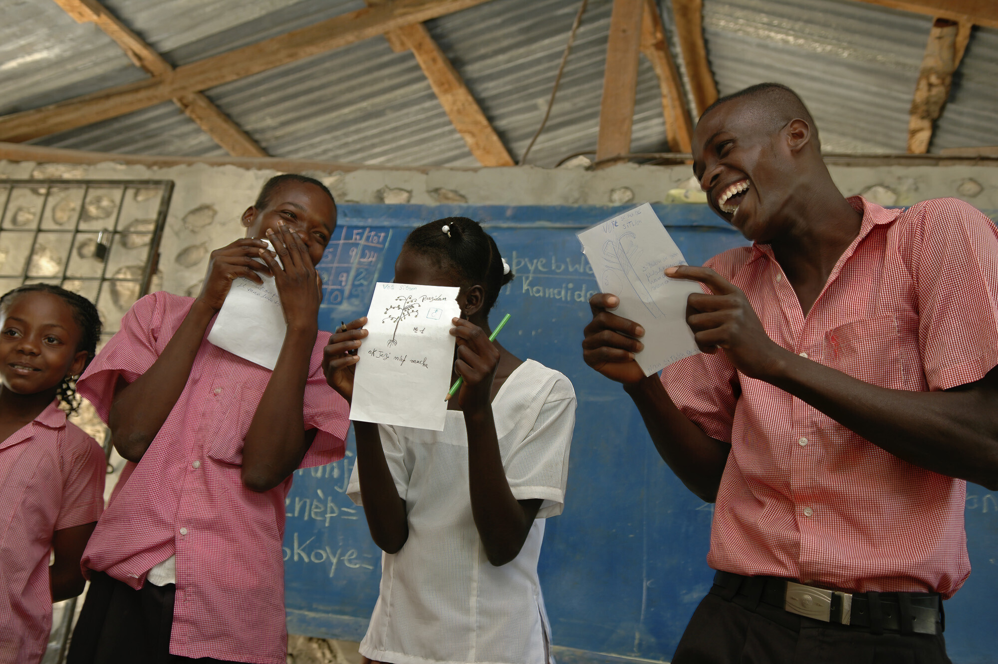 Four Haitian students stand in front of a blackboard and laugh