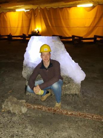 A man in a yellow hard hat squats in front a large block of salt