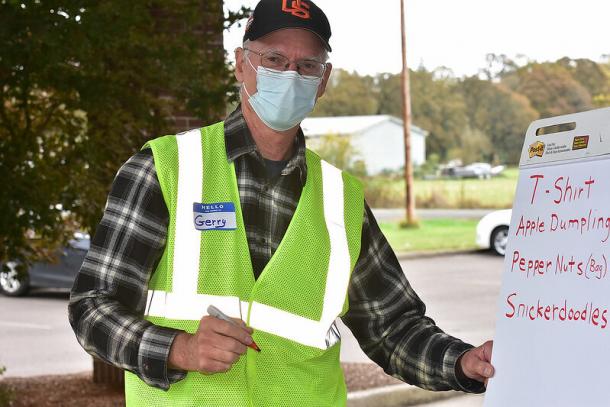 A man in a ball cap, face mask and a reflective green vest writes on a flip chart