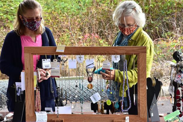 Two women in face masks look at a jewelry display at an outdoor event