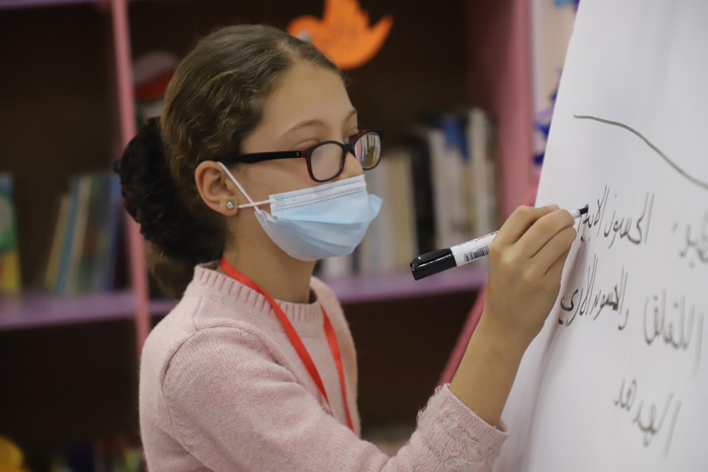  A girl in a face mask writes on a flip chart with a black marker