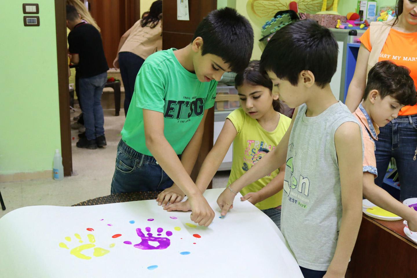 Three child doing finger painting on a large sheet of paper