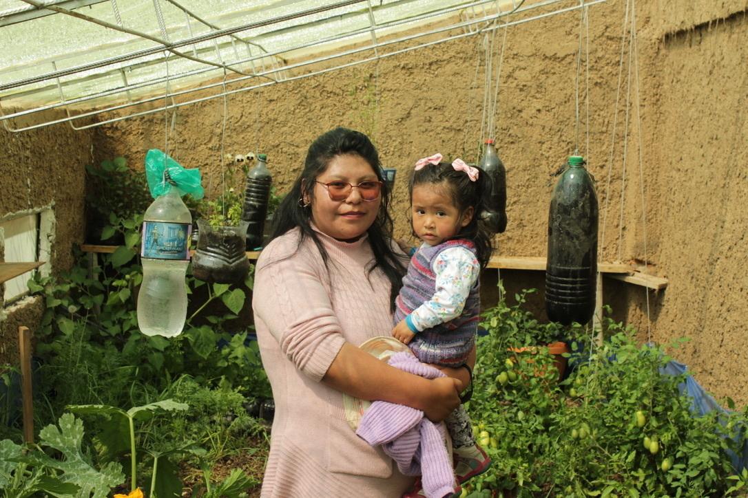 A mother holds her daughter in a greenhouse
