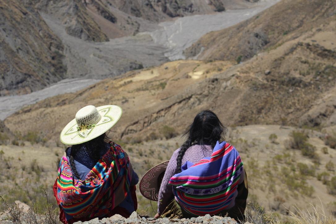 Two woman sit with their backs facing the camera look out on the mountains of Bolivia