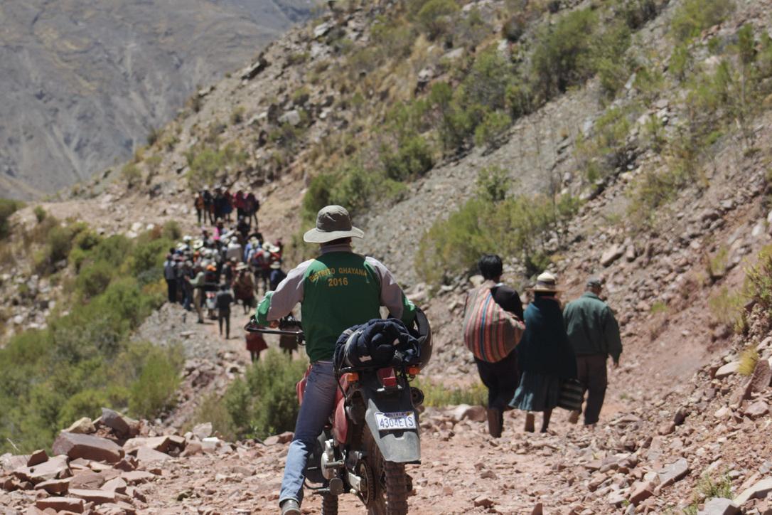 A person on a motorcylce follows a group of people on a rocky mountain path