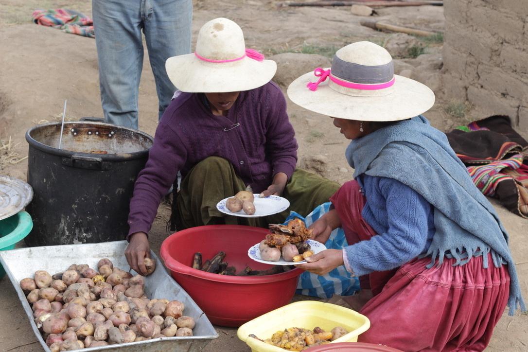Two Bolivian woman in large hats serve a meal of potatoes