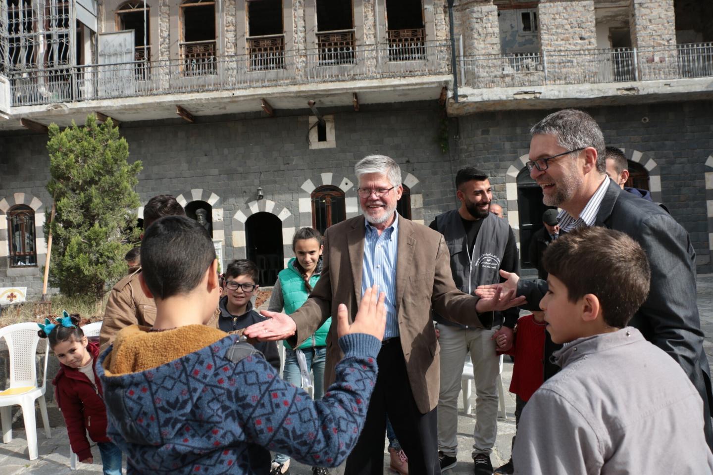 Two North American men greet Syrian children outside a stone building