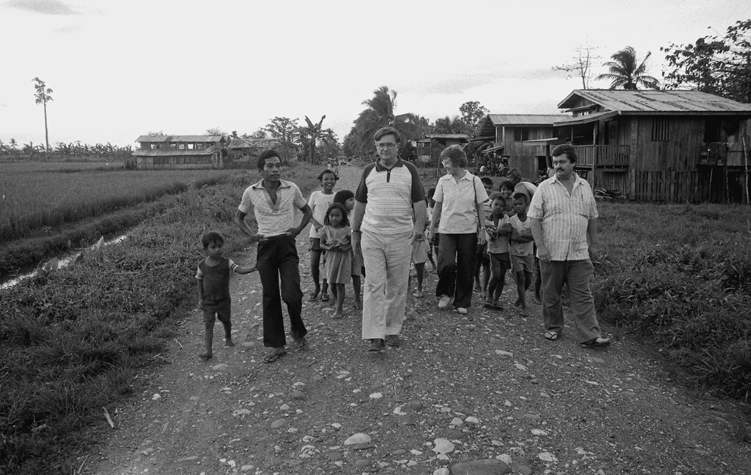 A black and white photo of a group of people walking in a Filippino village