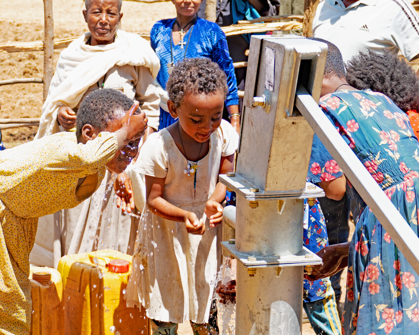 A group of children gathering water around a water pump