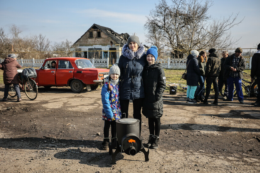 This family* in a village recovered from Russian military control in Ukraine's Kherson region stand with the wood stove they received from MCC partner Charitable Foundation Uman Help Center (Uman Help