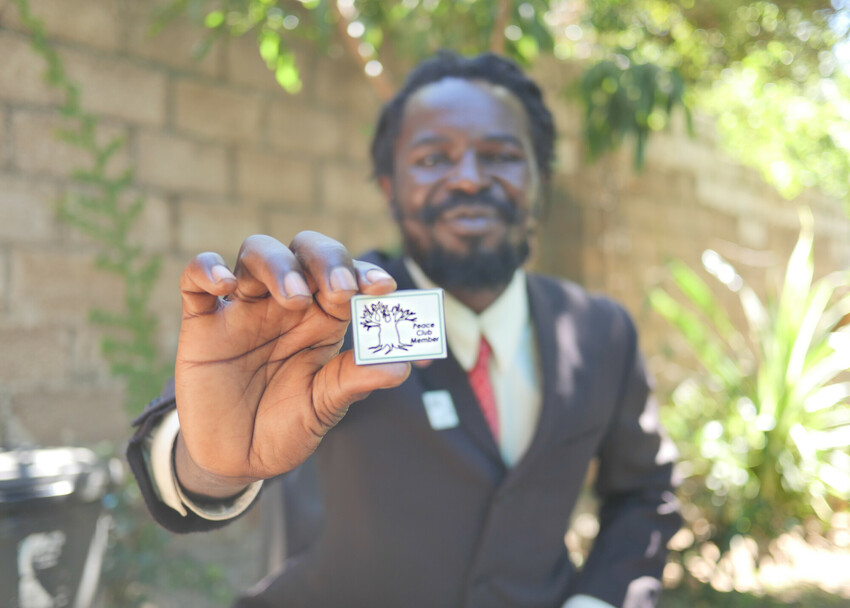 Zebron Mwale holds his badge to signify his Peace Club membership in April 2021. Mwale joined a Peace Club program while serving his sentence in a Zambian prison. He credits Peace Clubs with changing