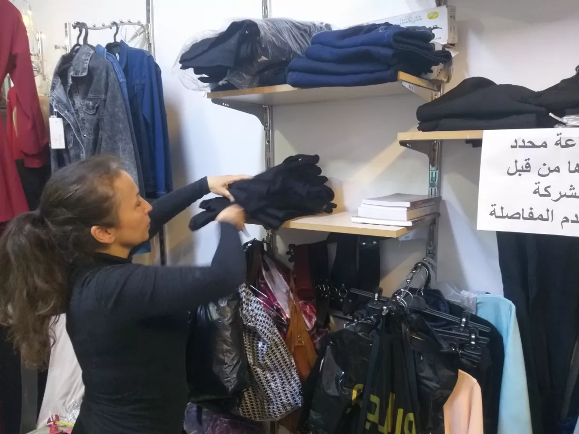 A woman organizes clothing on a shelf in a store
