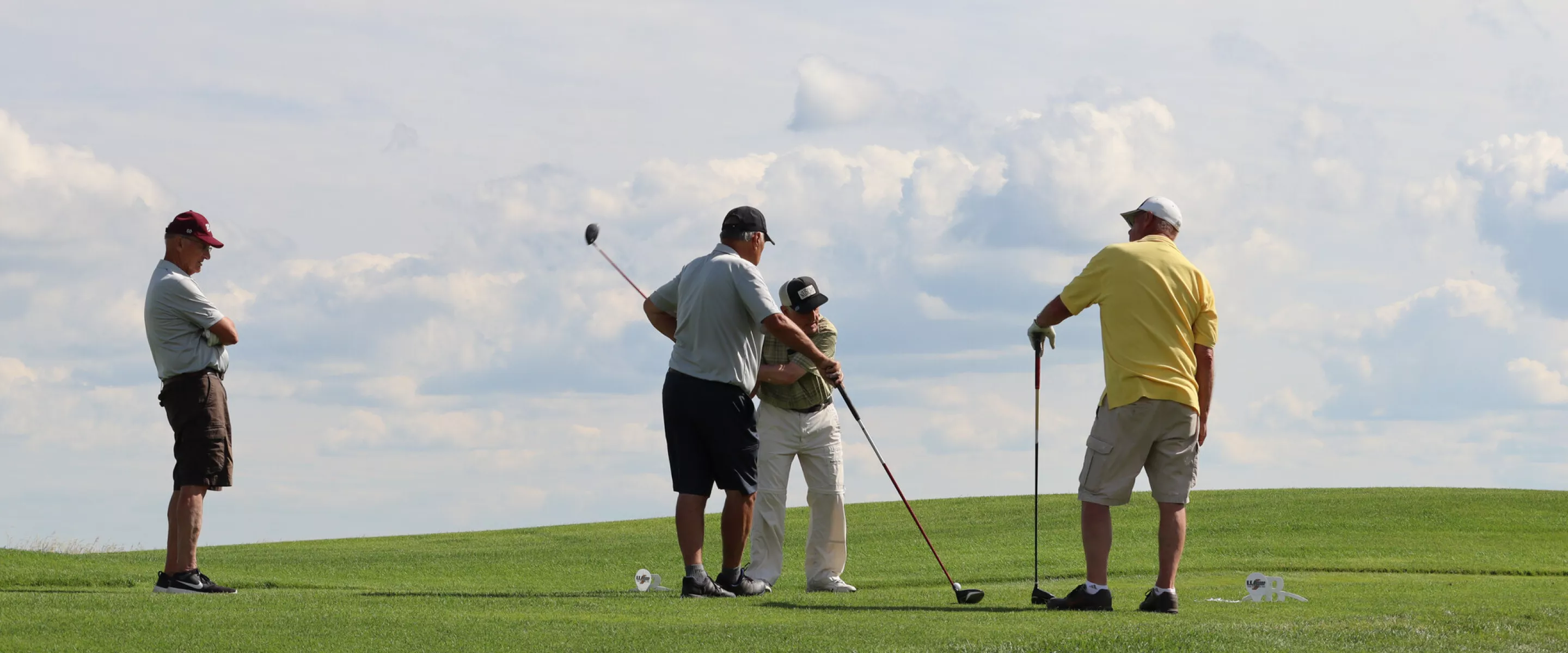 four golfers on a green in front of a blue sky