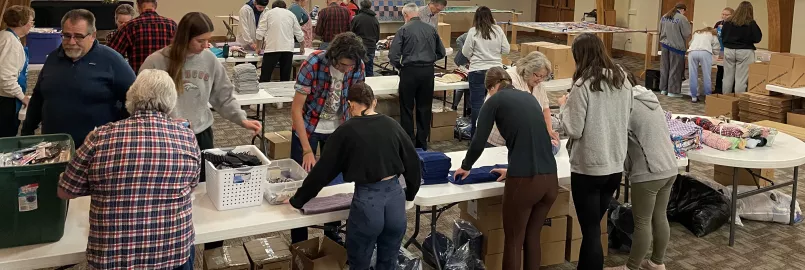  A group of volunteers assemble hygiene kits in large room.