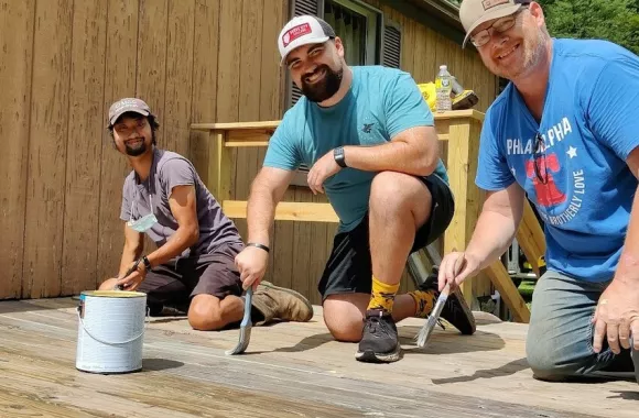 Three men work on staining a wooden deck