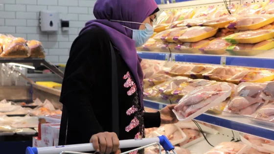 A woman in a purple hijab looks at the chicken section in a grocery store