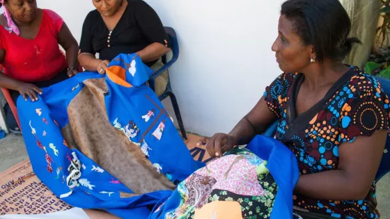 Three Colombia women sit and sew a comforter