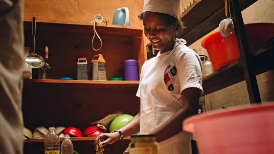 A Rwandan woman in a chef hat whisks something in a bowl