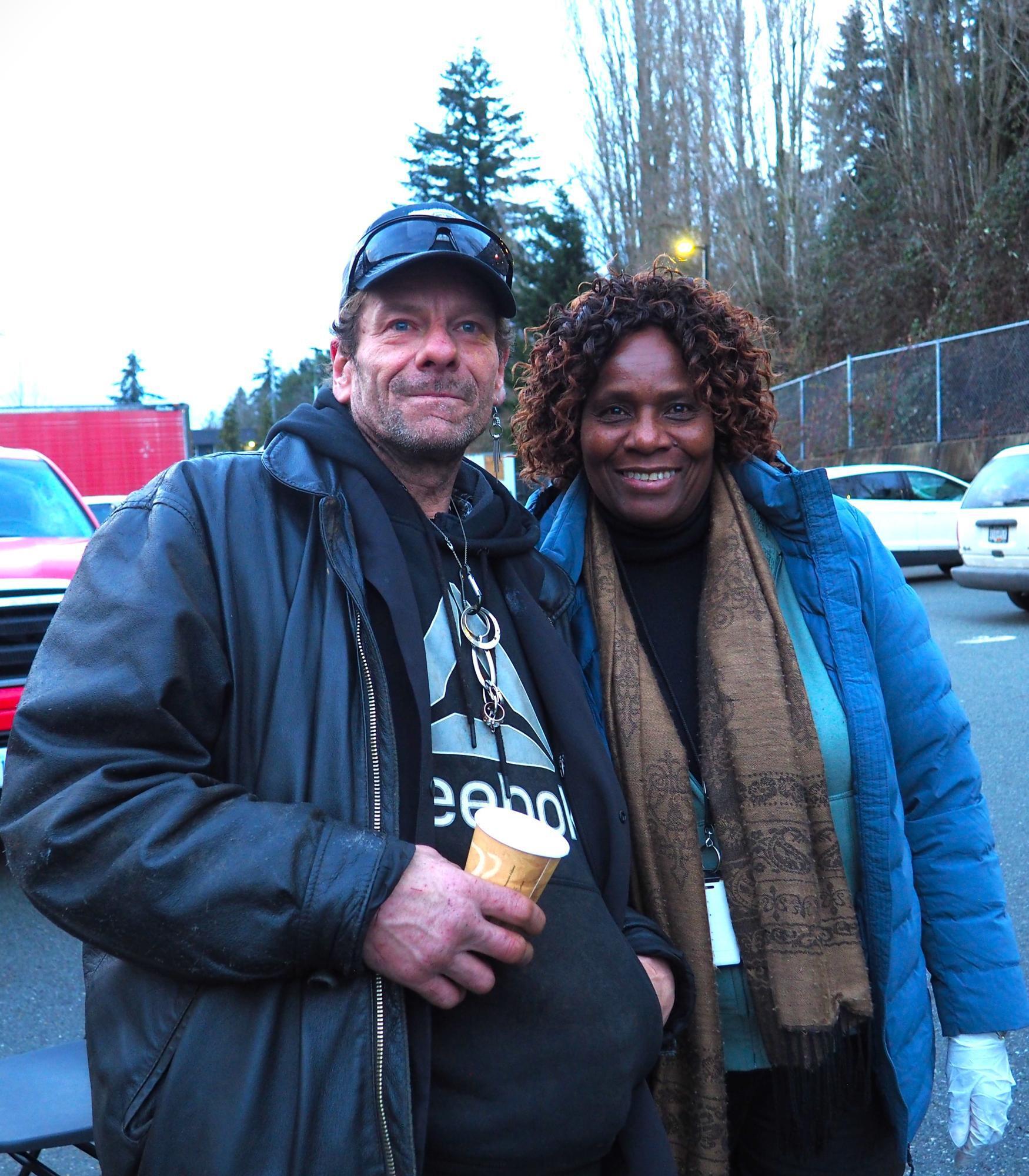 Two people standing side by side, one is holding a paper cup and the other is wearing a food glove.