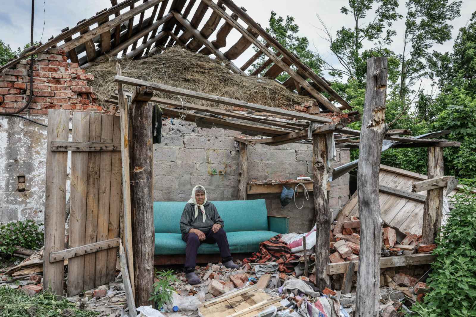 An elderly Ukrainian woman sit on a blue couch in the wreckage of her destroyed home