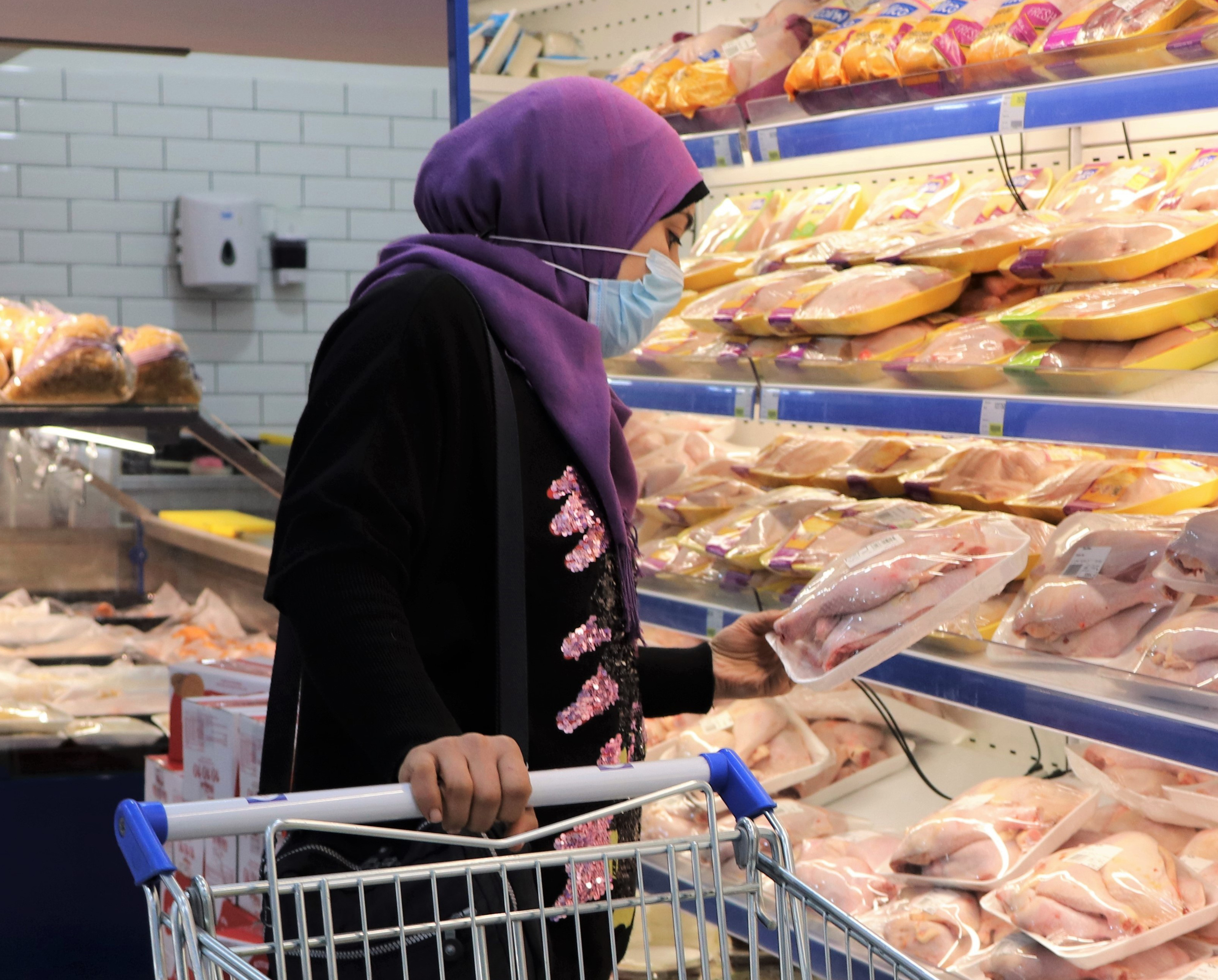 A woman in a purple hijab looks at the chicken section in a grocery store