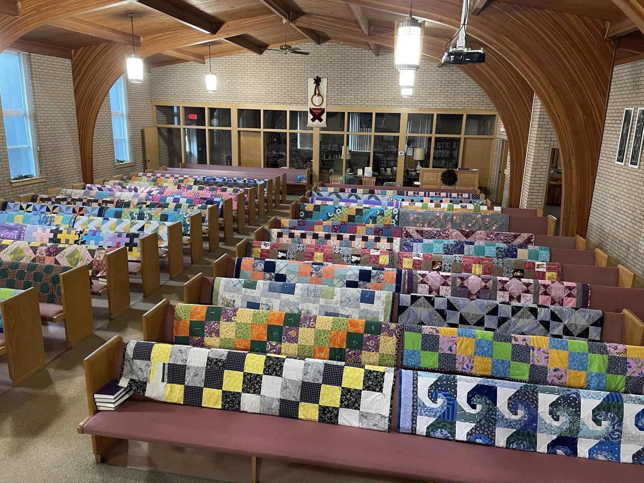 50 colorful comforters draped over church pews