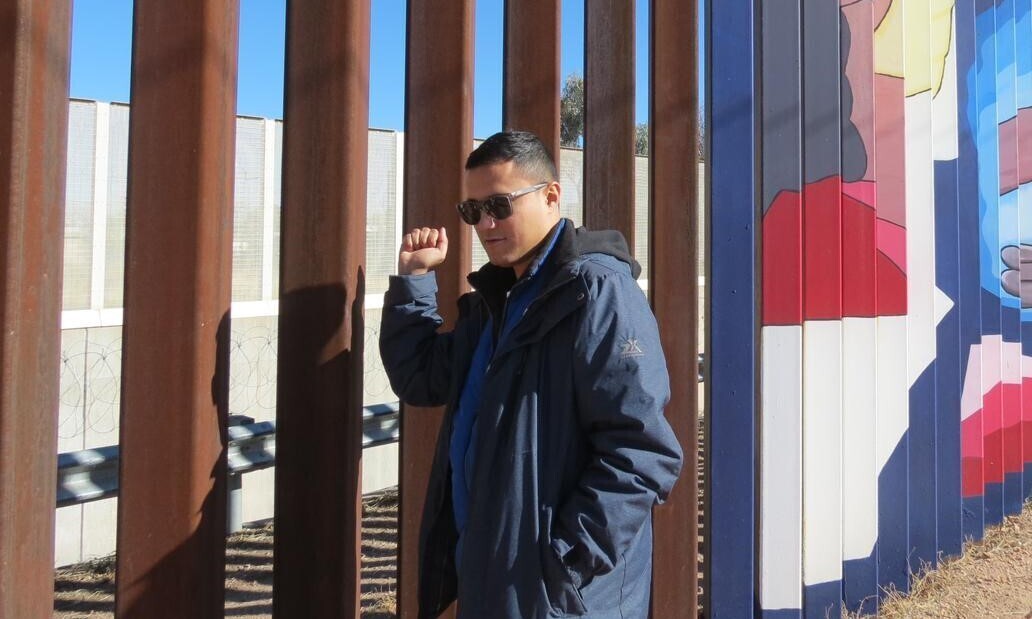 A man standing in front of a border wall