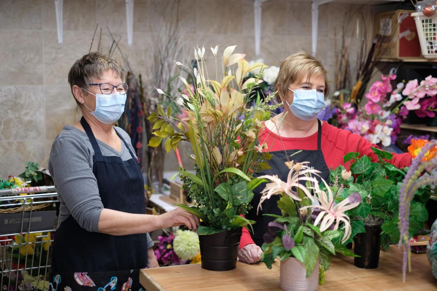 Two women in face masks work with plants in a thrift shop