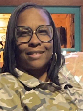A woman with short black hair and glasses wears a camo printed shirt