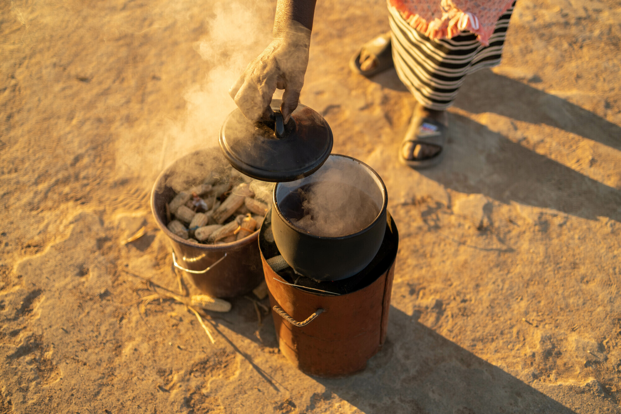 pot cooking on a fuel-efficient stove beside a bucket of corn cobs