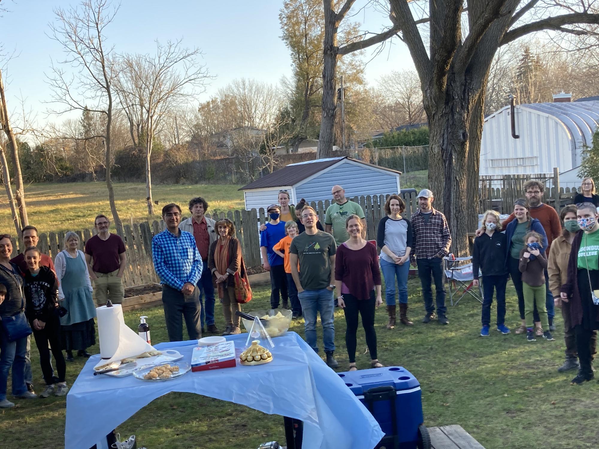 A group of people stand facing the camera in a backyard with a table of treats in the foreground.