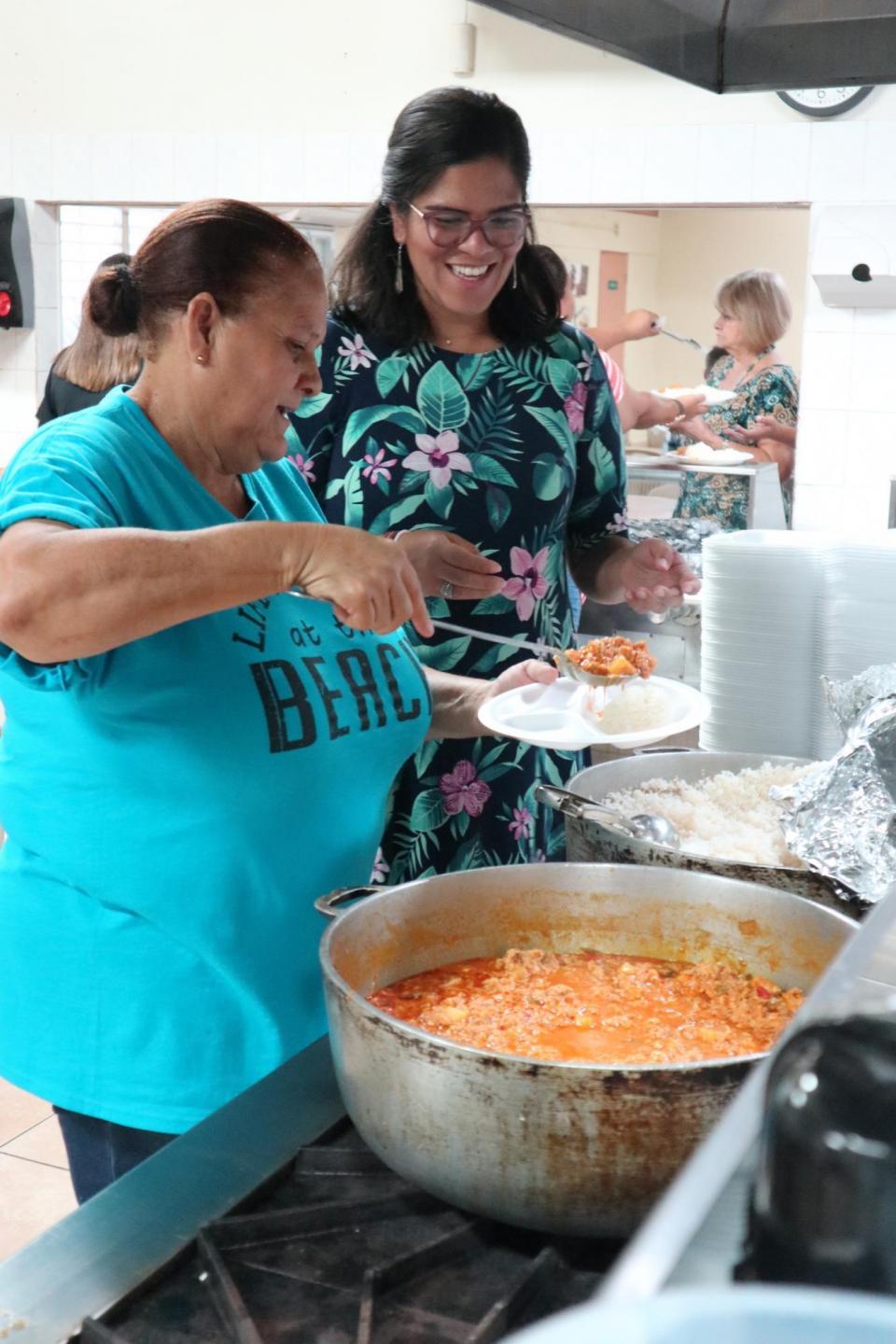 A woman dishes up some food on a plate for a young woman