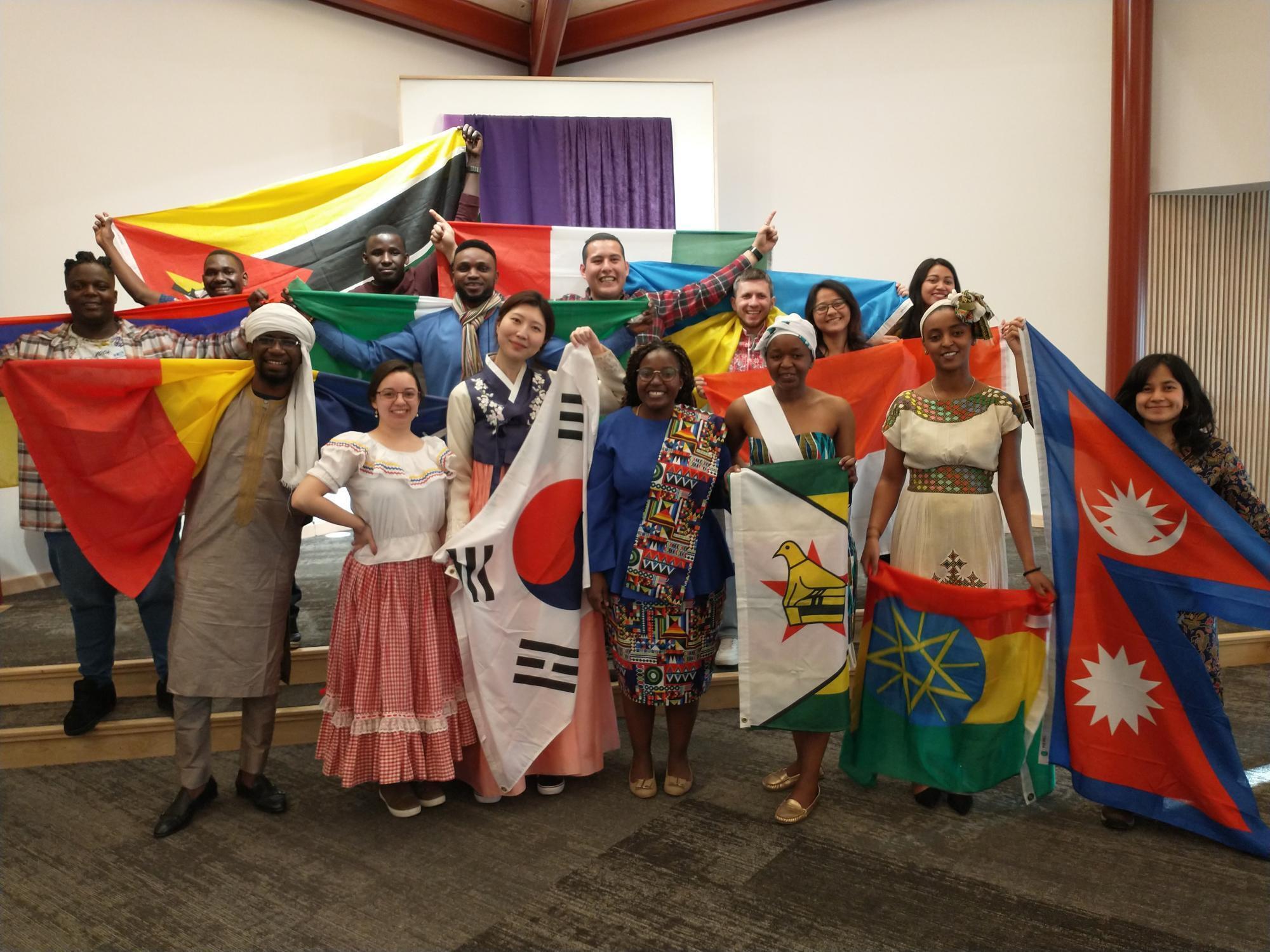 A group of young adults of different nationalities stand together. They are holding their country flags and dressed in traditional outfits.