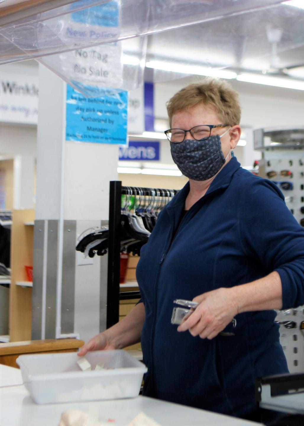 A woman with short hair, glasses and a face mask works at a thrift shop
