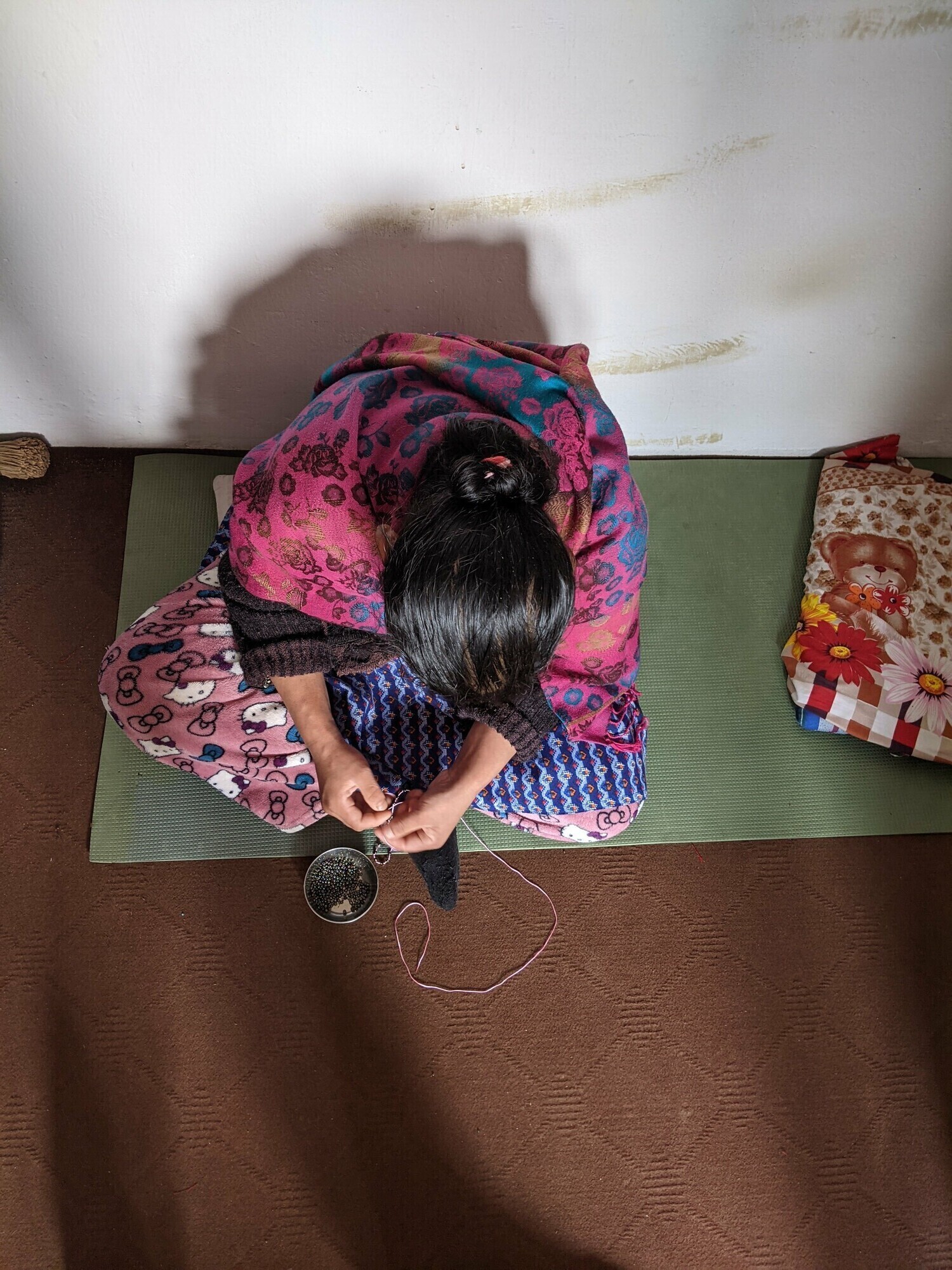 Woman sitting on a mat threading a needle.