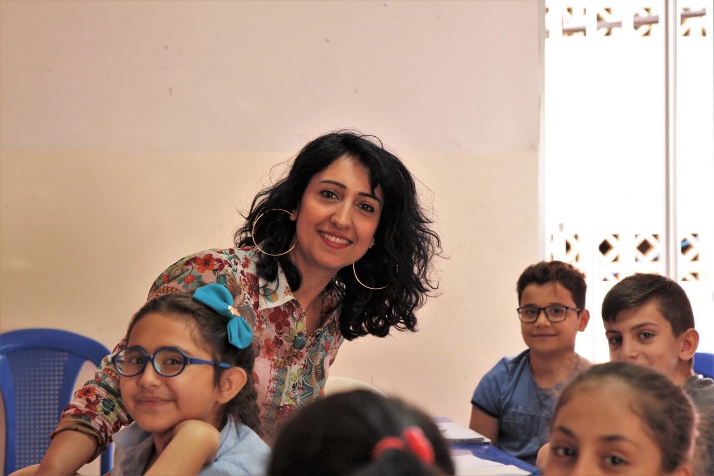 A teach smiles at the camera while leaning over a group of students