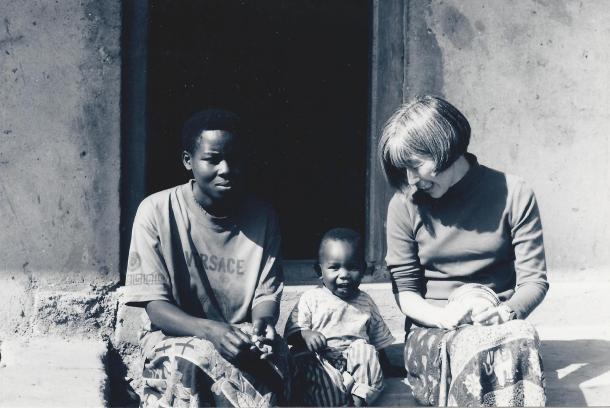 A black and white photo of three people sitting on a step in front of a doorway in Uganda.
