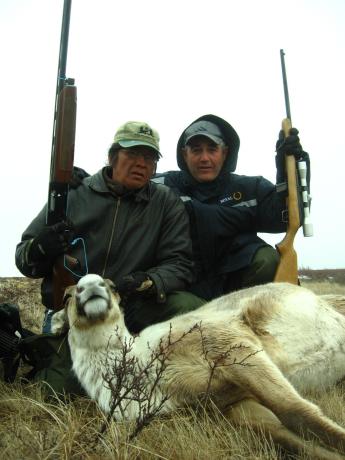 Two hunters pose with rifles and a dead animal