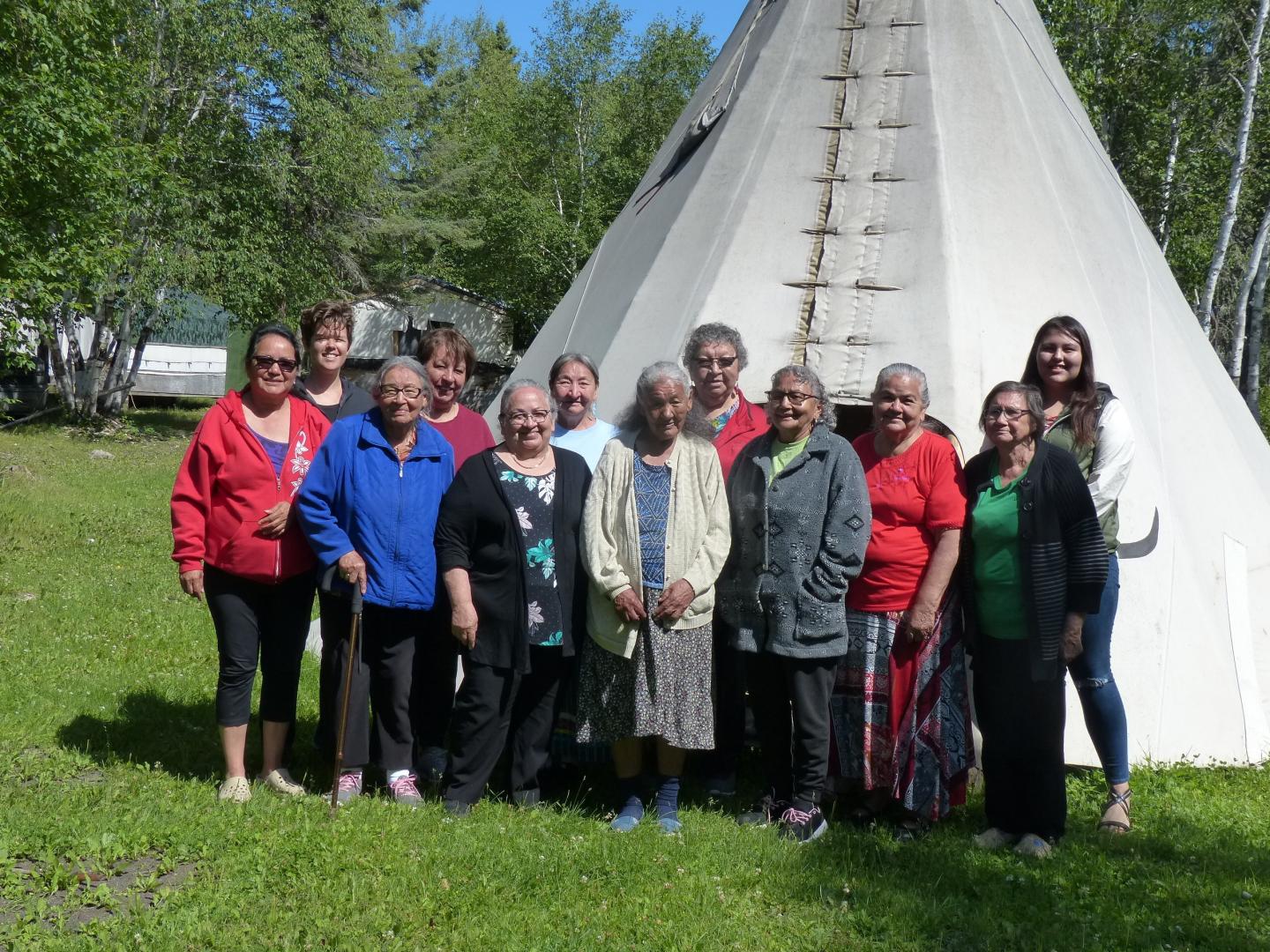 A group of Indigenous people stand in front of a tipi 