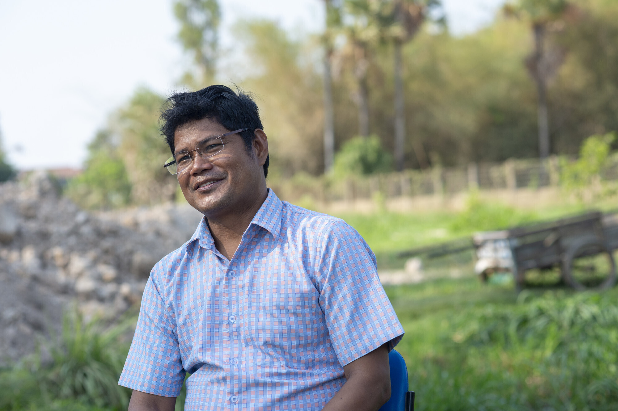 A protrait of a Cambodian man in a blue button-down shirt and glasses.