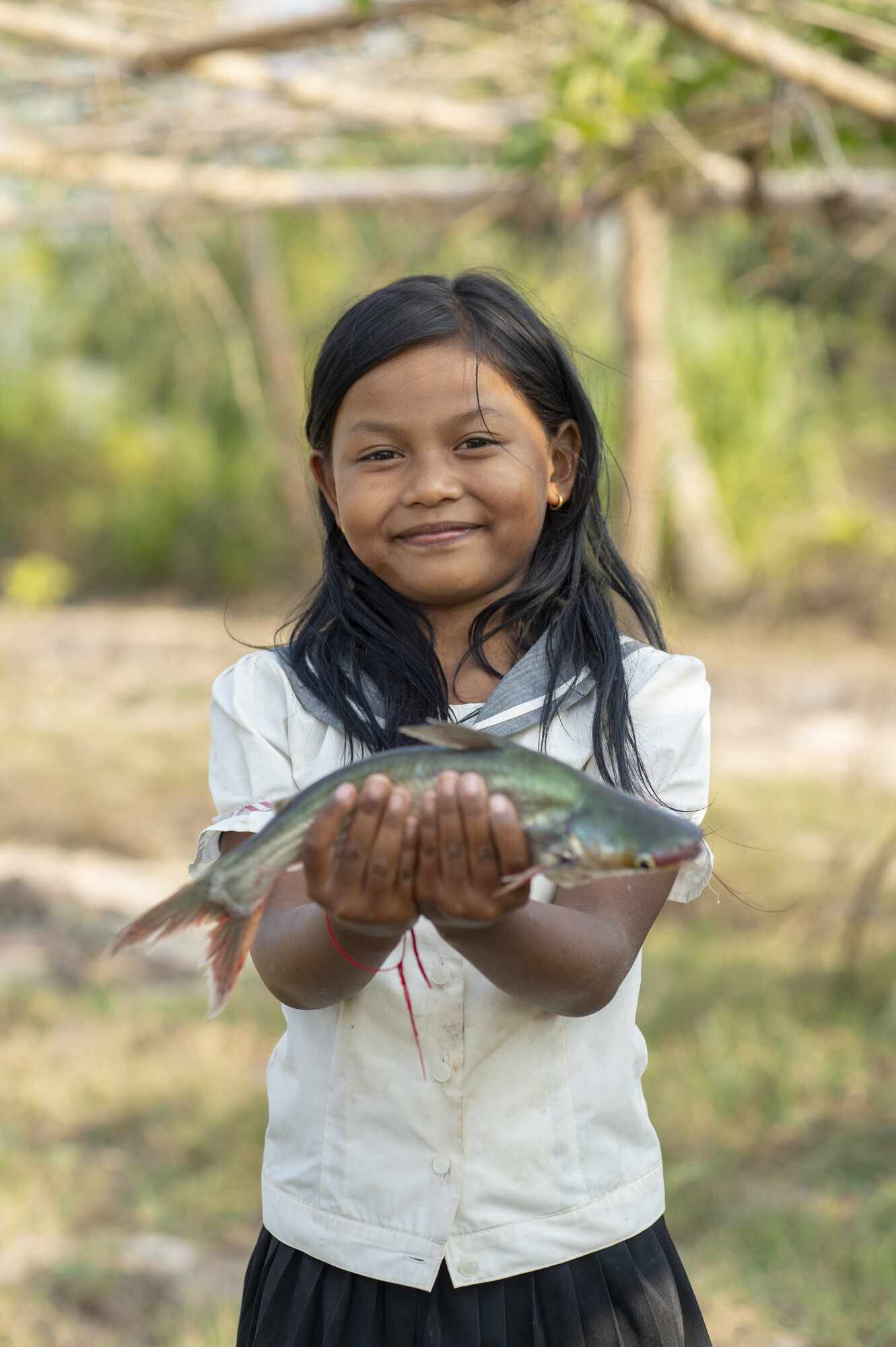A portrait of a young Cambodian girl holding a fish