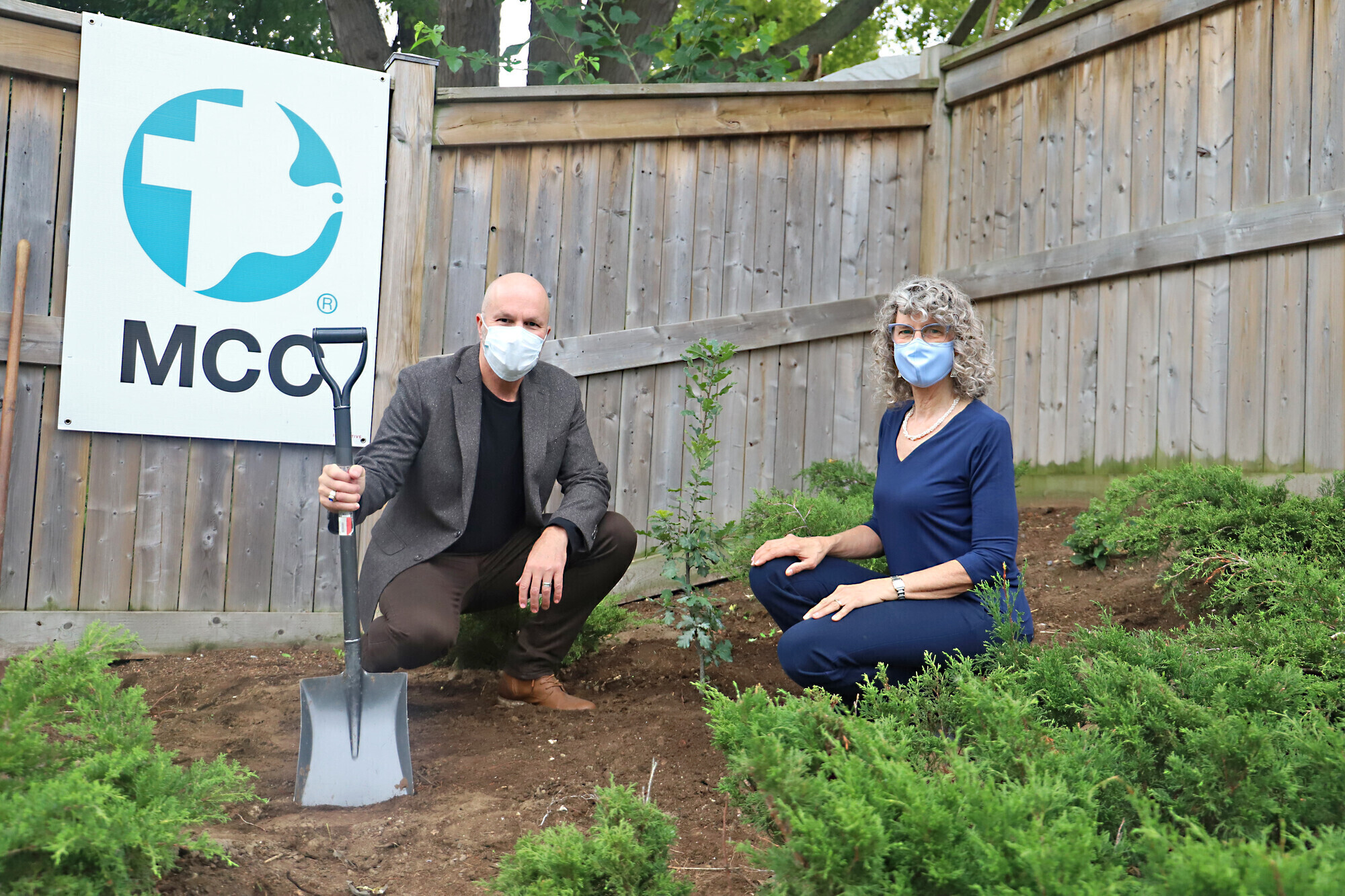 A man and woman planting a tree in front of an MCC sign
