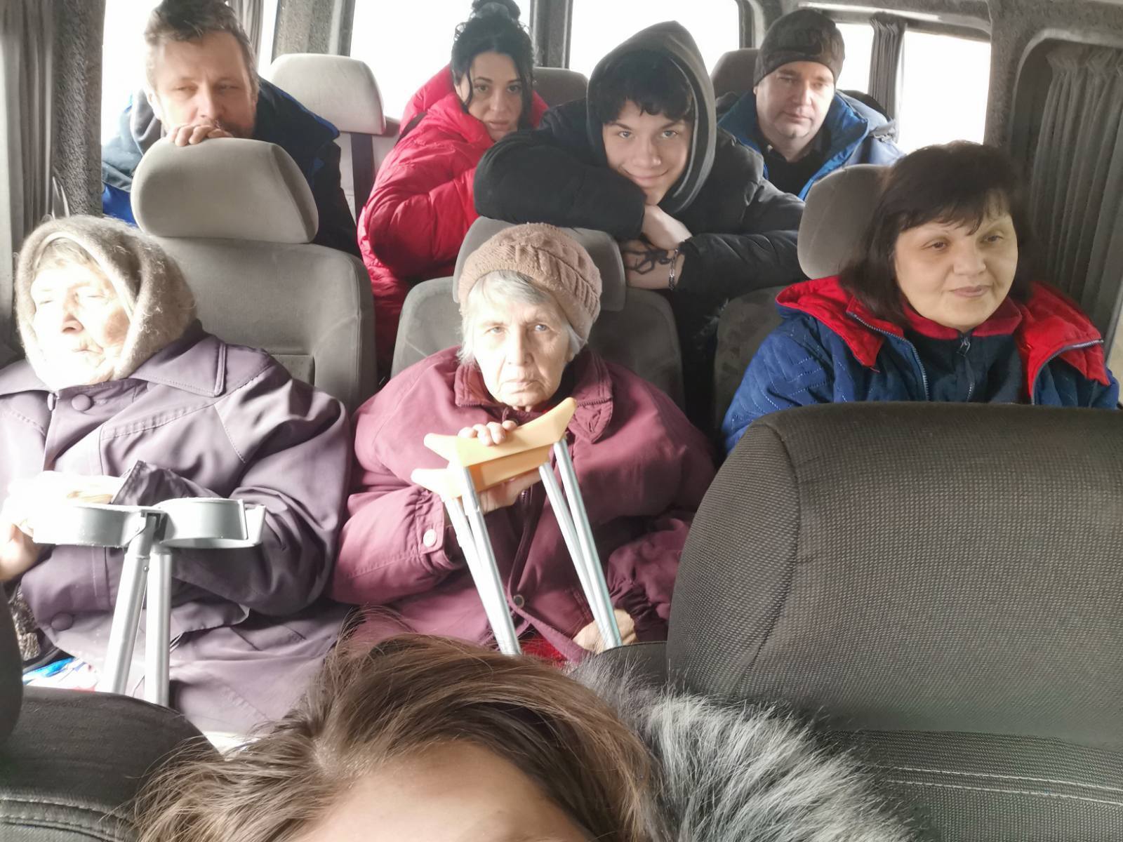 A group of people in winter clothes sit in a van